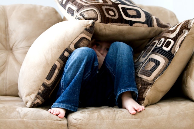 child hiding underneath pillows with only small portion of face looking out