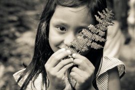 young girl playing in nature holding a leaf branch by her face
