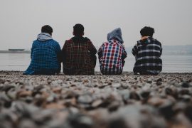 photo of a group of teenaged boys sitting on the beach in hoodies with looking at the ocean
